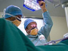 Two medical professionals in PPE looking down at a patient in a hospital room.