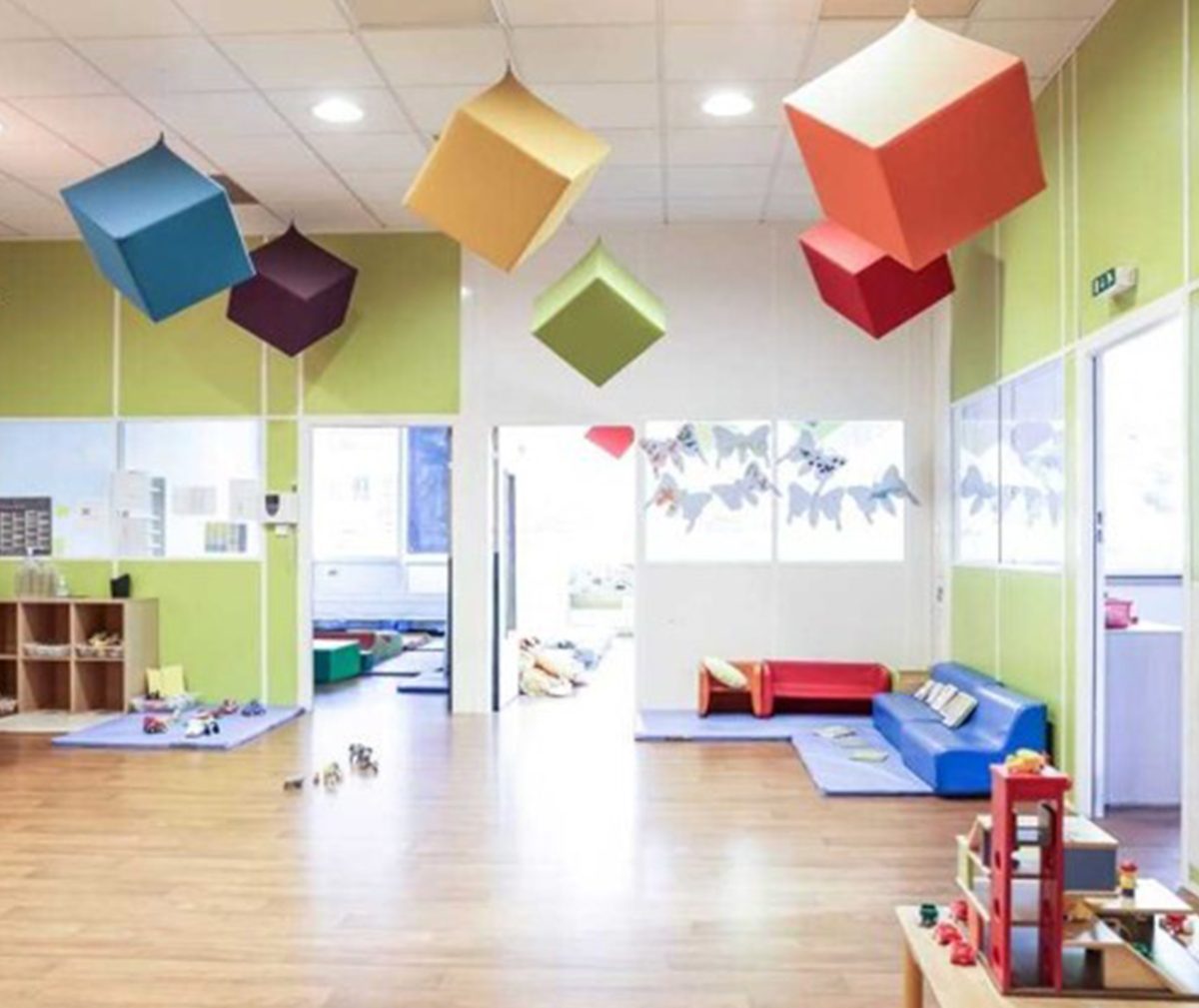 A colourful preschool reception, with blue, red, green, yellow and purple cubes hanging from the ceiling. The furniture is colourful and playful, with toys scattered throughout the room.