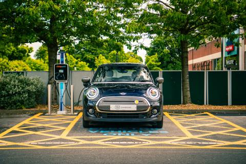 An electric car charging in a parking lot, surrounded by greenery.