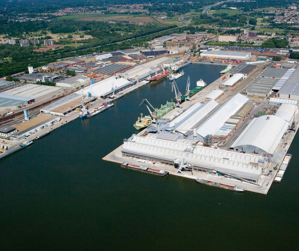 An aerial view of an expansive industrial port complex. The port features numerous docks, warehouses, and storage tanks along its waterfront.