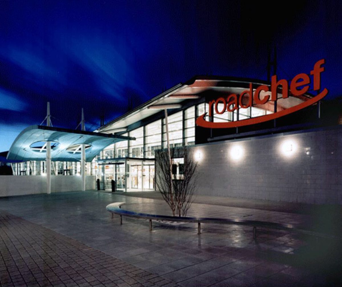 A Roadchef motorway station at night. The building's bright lights forms a stark contrast with the dark sky.