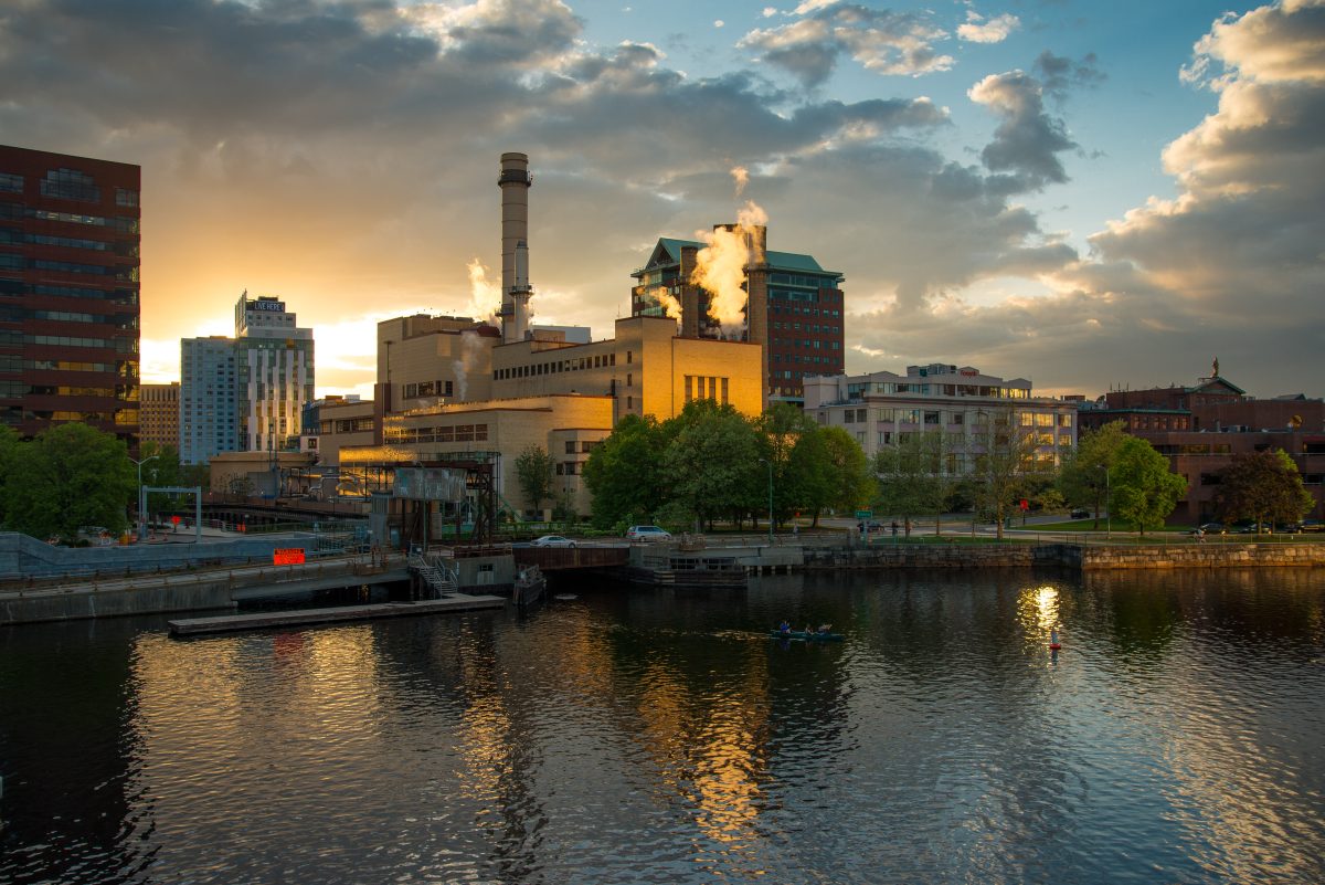 Serene cityscape showing a factory across a river. Its modern architecture blends in with the local buildings.