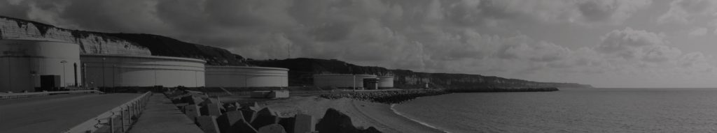 A black and white image of a factory by the seaside.