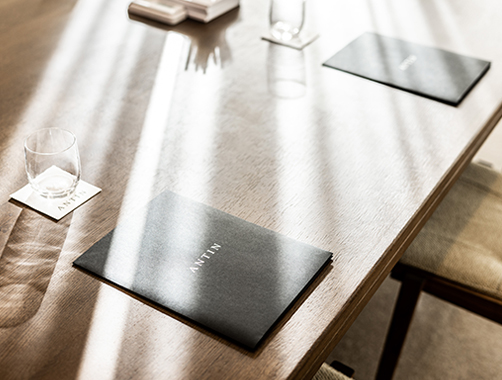 An elegantly set meeting table bathed in natural sunlight. The table features two black folders with the word 