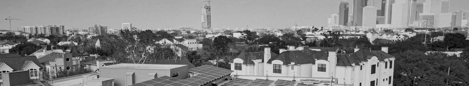 Black and white image of a suburban area with solar panels on the roofs of houses. High-rise city buildings are visible in the background.